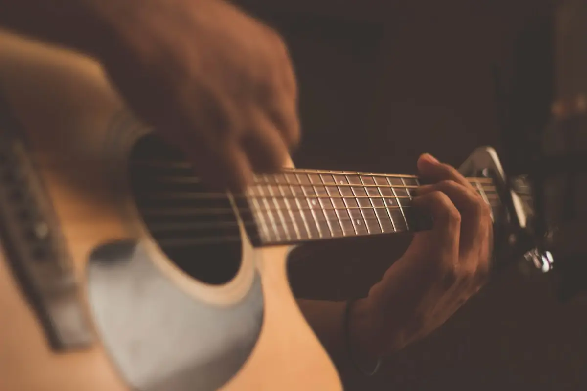 How to Reduce Admin Work as a Music Studio Owner (Systems That Actually Free Up Your Time) 2 Close-up of a person playing an acoustic guitar, with one hand strumming the strings and the other pressing down on the frets. The image has a warm, soft focus, emphasizing the hands and guitar.